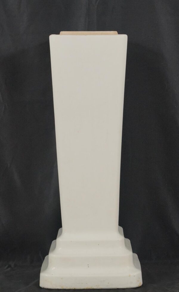 White ceramic sink pedestal base with a tapered column shape and stepped footed base, shown front view with the top opening visible.