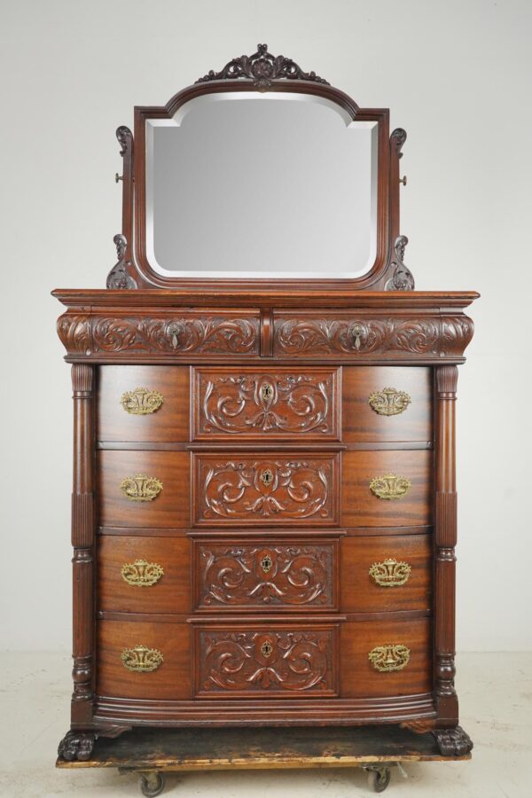 Victorian dresser in dark wood tone with a beveled mirror, carved details, and four drawers with antique brass hardware.