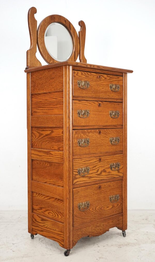 Tall Eastlake oak dresser with a beveled mirror, five drawers, brass pulls, and caster wheels.