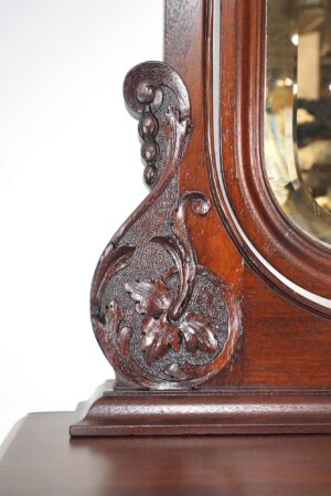 Close-up of a Victorian mahogany dresser showing the carved wood corner beside a beveled mirror.