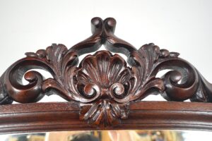 Close-up of the carved Victorian dresser crest in dark wood tone with a beveled mirror edge below.