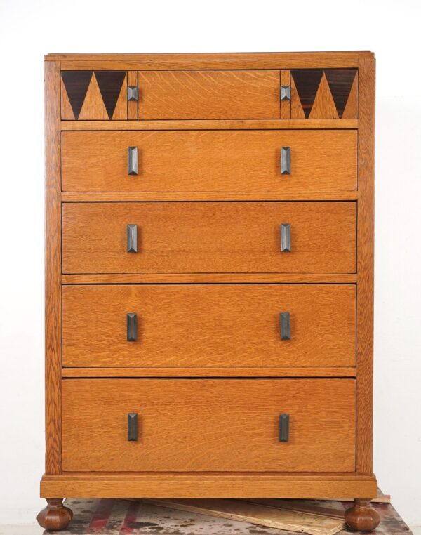 Five-drawer oak dresser with geometric top drawer inlays and dark handles, shown front view on turned feet.