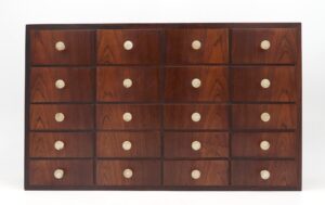 Mid century wall cabinet with twenty small drawers in a four-by-five grid and round brass knobs.