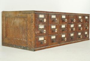 Antique tabletop card catalog cabinet with eighteen drawers, brass label holders, and knobs, shown at an angle.