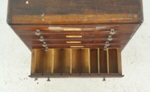 Top view of a vintage industrial shop counter display cabinet with a dark wood tone finish, showing the underside with brass hardware and open drawer compartments.