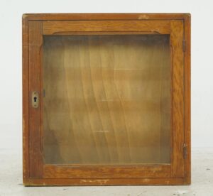 Vintage display cabinet with a glass front, medium wood tone frame, and brass keyhole hardware.