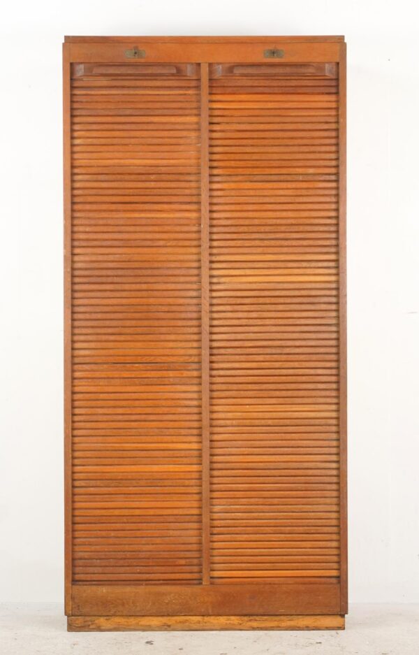 Tall mid century file cabinet with double tambour doors and top latches, shown closed in a dark wood tone.