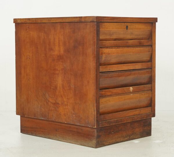 Mid century wood filing cabinet shown at an angle with four stacked drawers and visible surface wear.