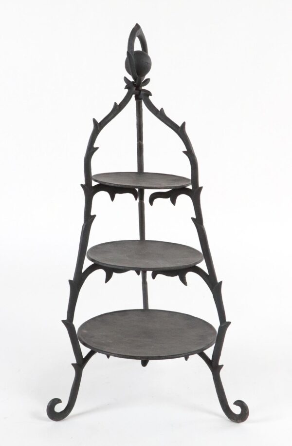 Art Nouveau cast iron three-tier display stand with an arched tracery frame, three round removable trays, and curled feet shown front view.