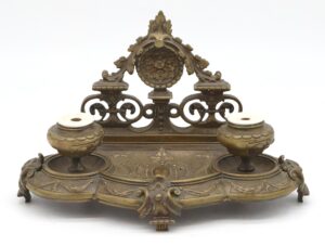 Victorian bronze double inkwell tray with two ceramic inkwells and an ornate raised back panel with scrollwork.