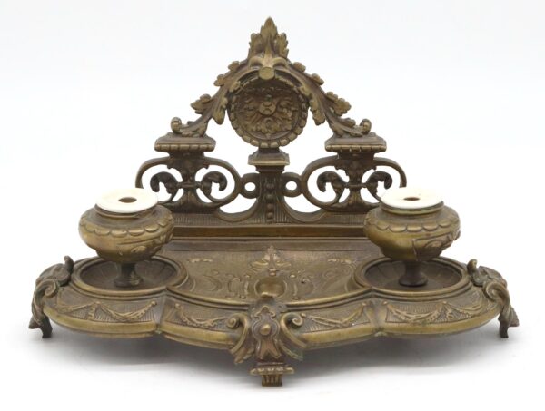 Victorian bronze double inkwell tray with two ceramic inkwells and an ornate raised back panel with scrollwork.