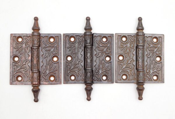Set of three Victorian cast iron butt door hinges with steeple tips, three knuckles, and four mounting holes each, shown front-facing with visible surface wear.