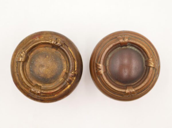 Pair of antique brass door knobs shown from the back, each with a round rosette and stepped circular bands, displayed side by side.