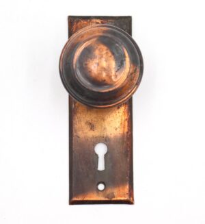 Vintage dummy door knob set with a concentric round knob on a rectangular back plate, shown front on and featuring a black and copper finish.