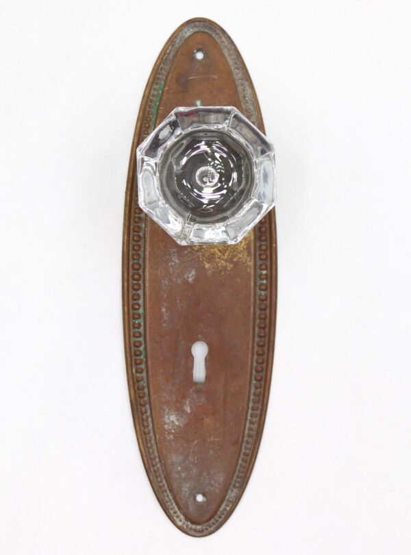 Octagonal glass dummy door knob on an oval brass back plate with beaded edging and a keyhole cutout.