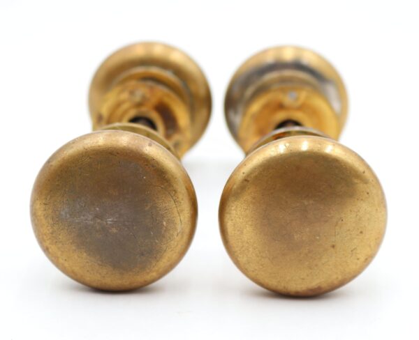 Two antique brass door knobs shown in close-up, with round rosettes visible behind each knob and noticeable surface wear from prior use.