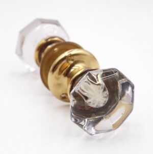 Close-up of an octagon glass passage door knob set with polished brass rosette and spindle, showing one clear knob and the matching brass fitting.