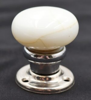 Vintage dummy door knob set with a round white milk glass knob on a nickel finish rosette, shown in close-up with visible tan veining.