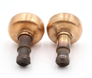 Pair of brass passage door knobs shown side by side, each with a cast iron latch end and visible surface wear from use.