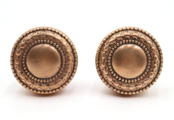 Pair of Victorian brass passage door knobs shown side by side, each with a round embossed face and polished finish.
