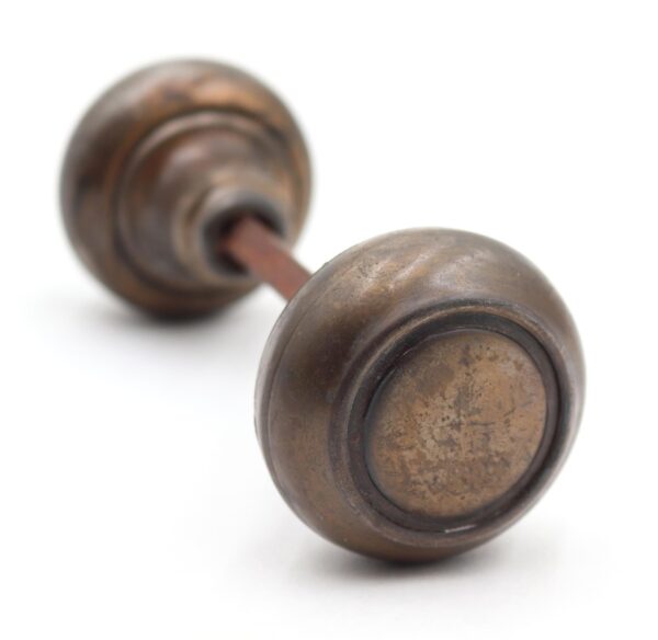 Pair of vintage passage door knobs with concentric fronts and a connecting spindle, shown in close-up with surface wear.