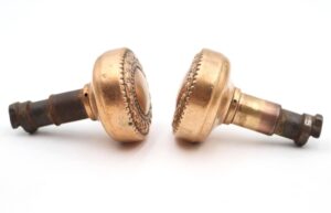 Pair of antique brass passage door knobs shown side by side, each with a cast iron latch end and visible surface wear.