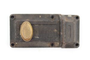 Vintage cast iron night latch with a brass thumb piece, shown from above with four mounting holes and surface wear visible.