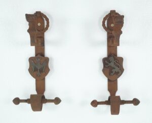 Pair of Gothic wrought iron double door pulls shown as a set, each with a central shield and round knocker; the left shield has an eagle emblem and the right shield has a lion emblem.