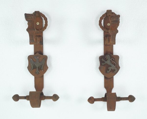 Pair of Gothic wrought iron double door pulls shown as a set, each with a central shield and round knocker; the left shield has an eagle emblem and the right shield has a lion emblem.
