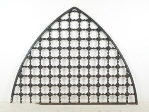 Arched wrought iron window grille with a square lattice pattern and worn frame, shown front on.