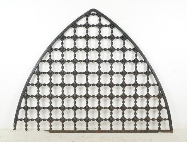 Arched wrought iron window grille with a square lattice pattern and worn frame, shown front on.