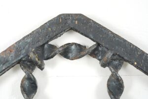 Close-up of an antique Gothic wrought iron window grille with an arched frame, showing surface wear and rust.