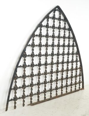 Antique Gothic wrought iron window grille with a pointed arched shape and square lattice pattern, shown in full with surface wear, rust, and a missing piece along the bottom frame.