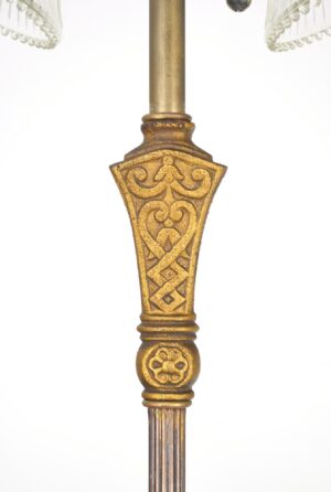 Close-up of an ornate gold-painted cast iron lamp base with a brass pole and part of two clear ribbed glass shades visible at the top.