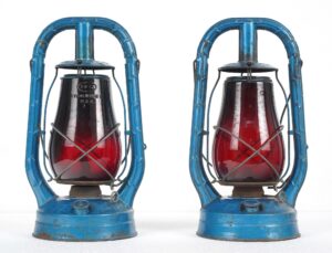 Pair of vintage kerosene lanterns with blue steel frames and red glass globes shown side by side.