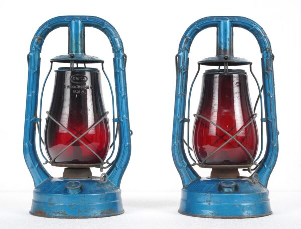 Pair of vintage kerosene lanterns with blue steel frames and red glass globes shown side by side.