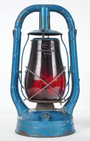 Vintage Dietz Monarch kerosene lantern with a blue steel frame and red glass globe, shown front view with the burner and protective wire guard visible.