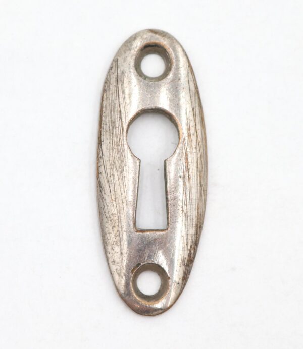 Oval keyhole cover plate with a keyhole opening and two screw holes, shown front on with visible surface wear and scratches on the nickel-finished brass.
