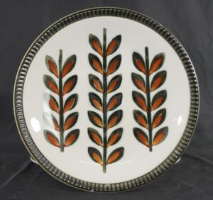 Ceramic plate with a Mid Century leaf pattern in black, brown, and white, shown from above with a ribbed rim.