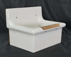 Vintage porcelain utility sink basin with a light wood strip on the front rim and two mounting holes in the back panel, shown in a three-quarter view with surface wear from prior use.