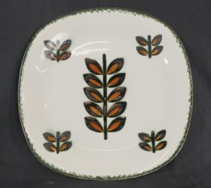 Ceramic plate with a central stylized leaf motif and four smaller matching motifs near the rim.