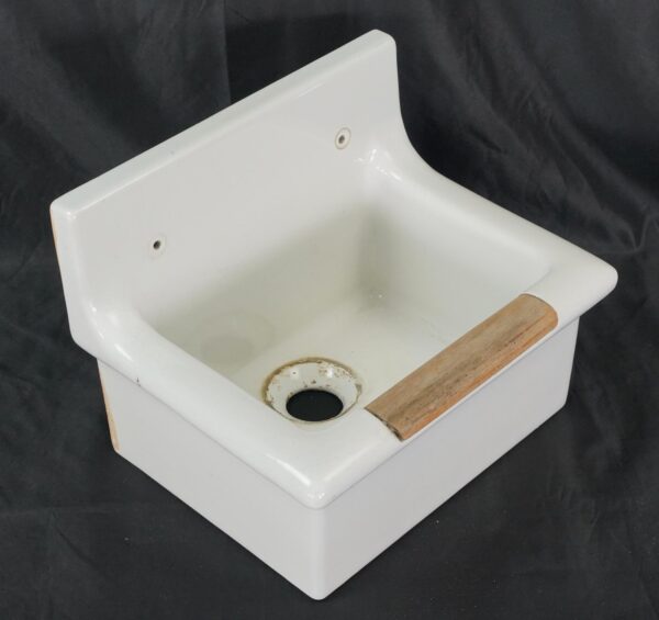 Vintage porcelain utility sink basin with a light wood strip on the front rim and a single drain opening visible inside.