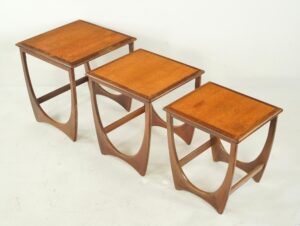 Set of three nesting tables with square tops and curved supports in a mid-century style, shown nested together in a dark and medium wood tone.