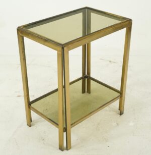 Mid-century side table with a polished brass frame and smoked glass shelves shown at an angle.