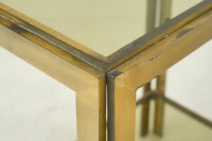 Close-up of a brass side table corner with a smoked glass top and visible surface wear.