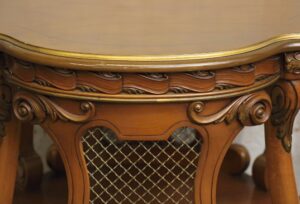 Close-up of a round side table with carved wood details, gold trim, and a wire mesh panel.