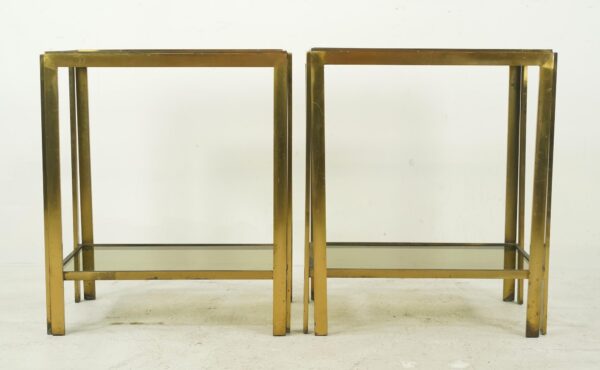 Pair of mid century side tables with polished brass frames and smoked glass shelves shown together in a front view.