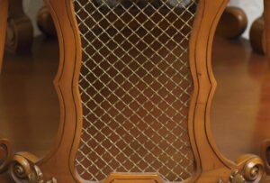 Close-up of a French side table with carved wood framing and a gold-toned metal mesh panel.