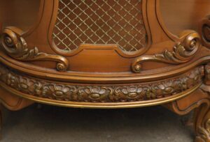Close-up of a round side table with carved wood detailing, wire mesh panel, and floral trim in a dark wood tone with gold accents.