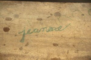 Close-up of a vintage school desk top with a pen groove, an inkpot hole, and student signatures visible in green.